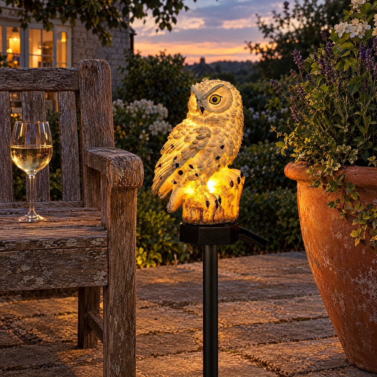 Gufo solar owl light beside a teak bench on a stone patio in the evening