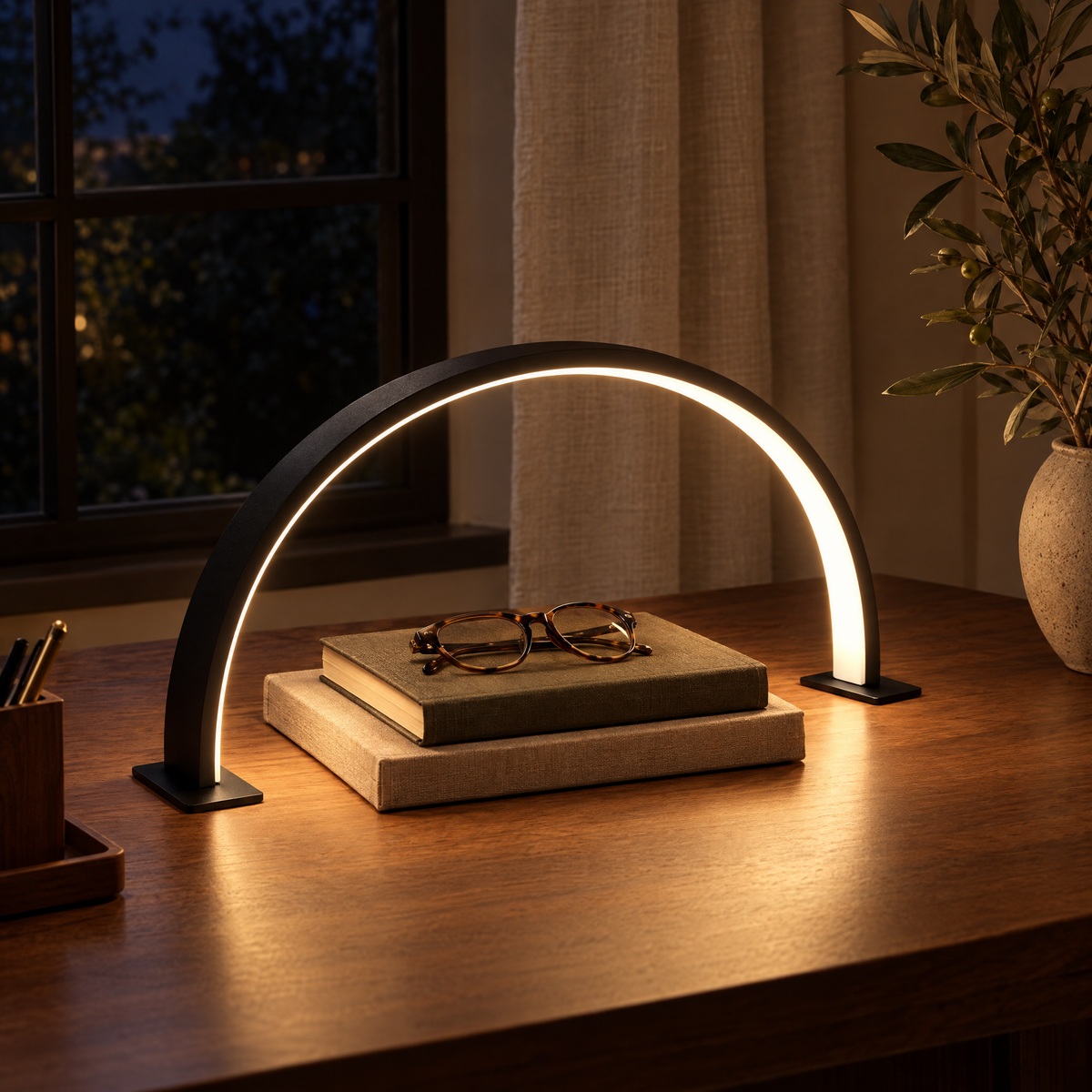 Black Luna half-moon lamp glowing over books on a walnut desk at night